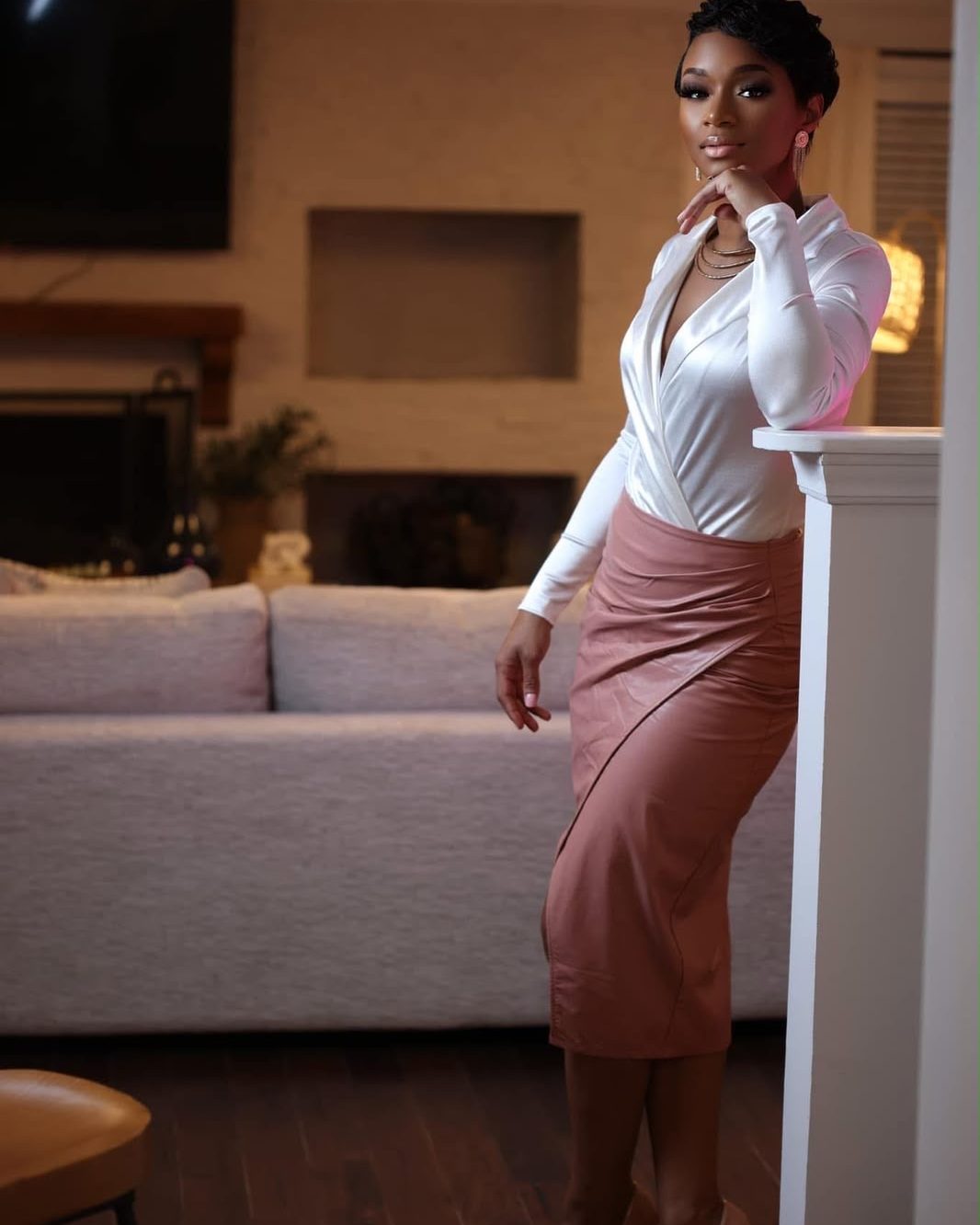 Brandy Tyson-Cummings at home in a white blouse and rose skirt, leaning against a mantel