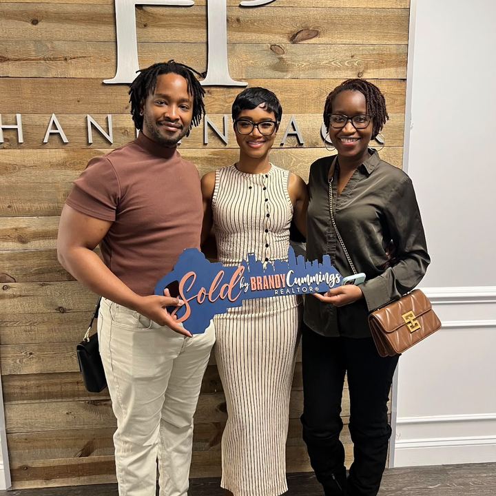 Burman and Tysheika Bedford with Brandy at closing, holding a ‘Sold by Brandy Cummings’ sign