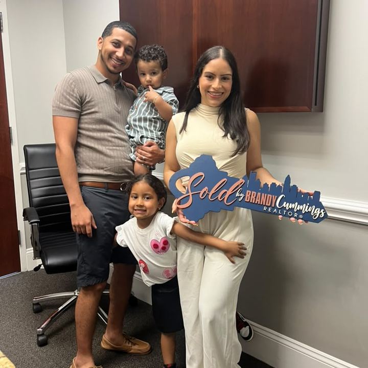 Rob and Ericka Torres with their two children at closing, holding a ‘Sold by Brandy Cummings’ sign